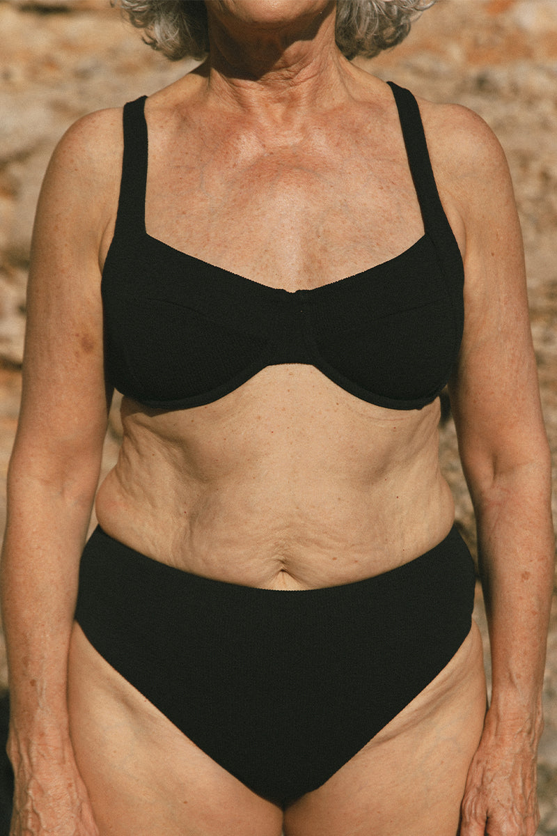 Older woman standing on the beach wearing Black Bikini AQVA Swimwear